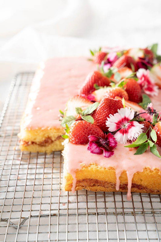 Strawberry Honey Bun Cake on the cooling rack with pink icing topped with strawberries and pink edible garnishes.