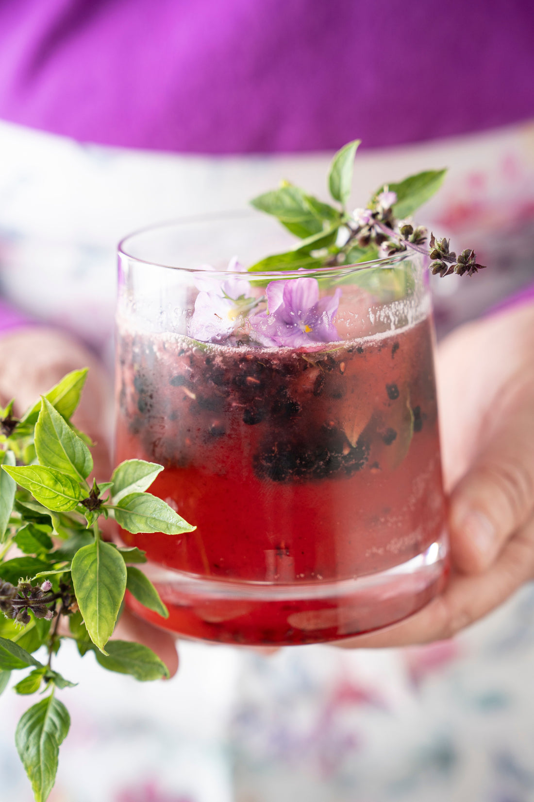 Someone holding a blackberry bourbon drink with a blackberry bramble.