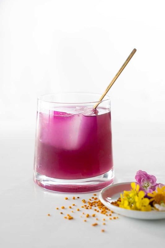 Butterfly pea flower cocktail next to bee pollen and flowers