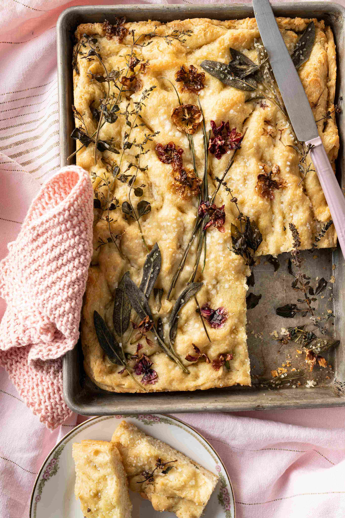 Flower focaccia on a baking tray with a pink knit blanket and butter knife.