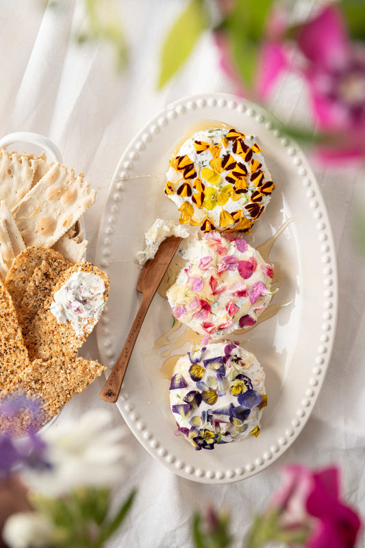 Goat cheese and honey board decorated with flower garnish.