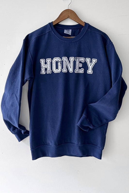 Navy blue varsity sweatshirt with Honey in all caps and faded lettering hanging against a white background.
