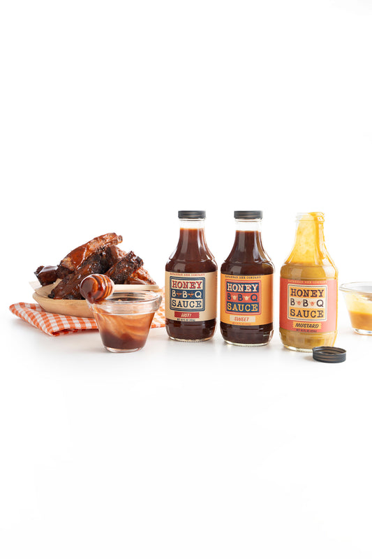 BBQ Collection lined up next to a plate of ribs and a glass cup filled with sauce