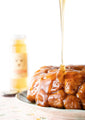 Monkey bread on a plate being drizzled with orange blossom honey with the 12 ounce jar in the background.