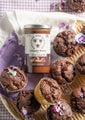 Triple chocolate muffins in a basket with a purple napkin next to a 12 ounce whipped honey with chocolate jar.