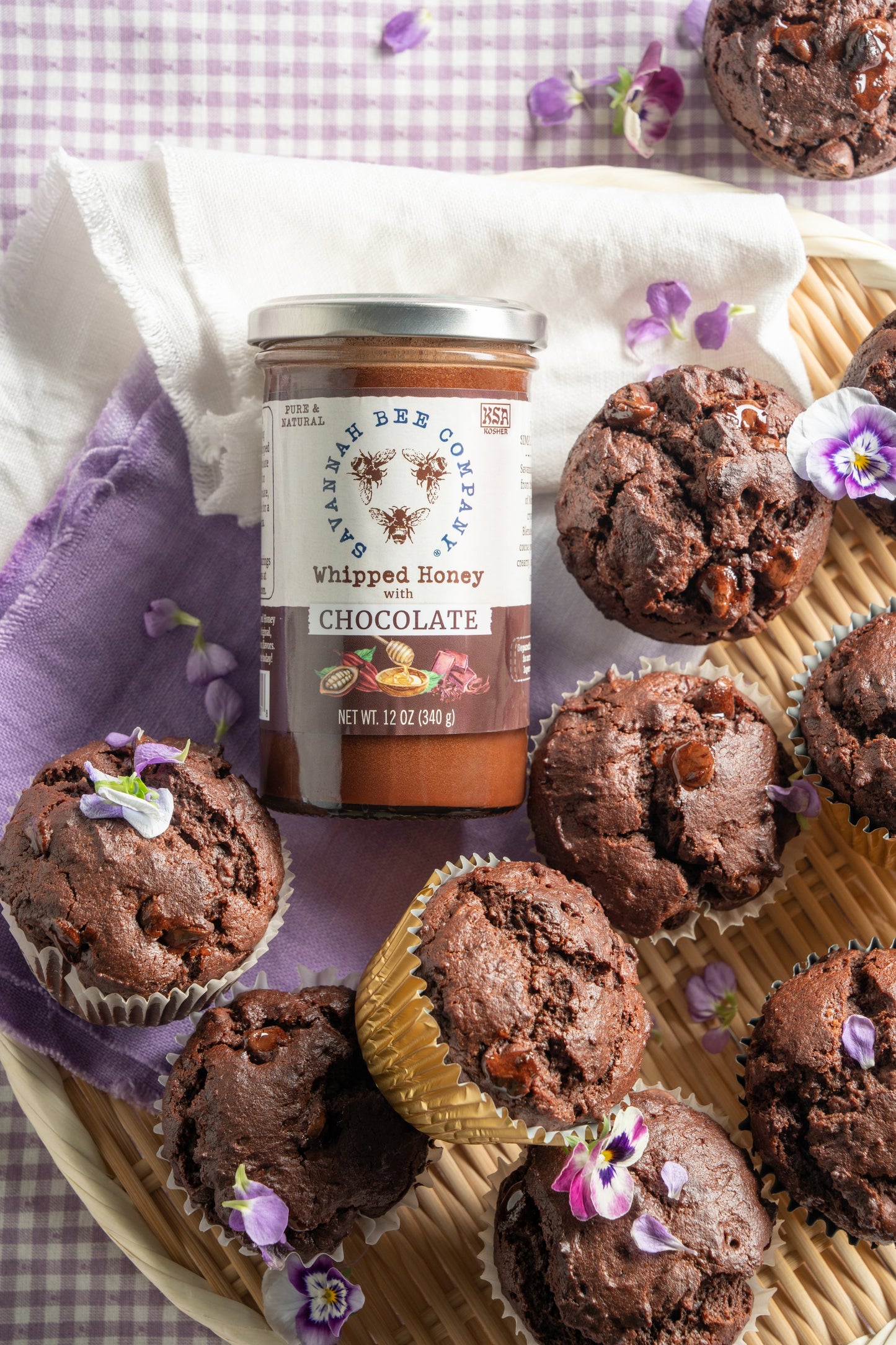 Triple chocolate muffins in a basket with a purple napkin next to a 12 ounce whipped honey with chocolate jar.
