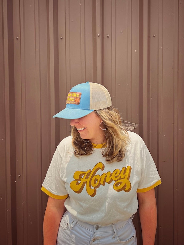 Blue save the bees hat on a model looking to her right against a brown wall