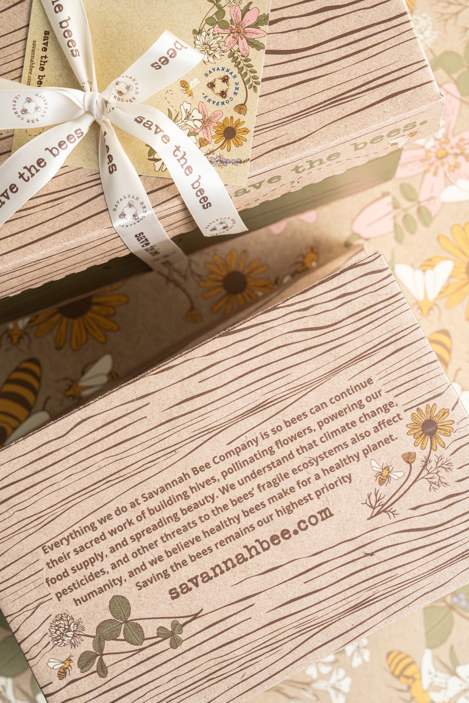 The bottom of a gift box with a quote and the Savannah Bee Company website next to a closed gift box tied with a save the bees ribbon