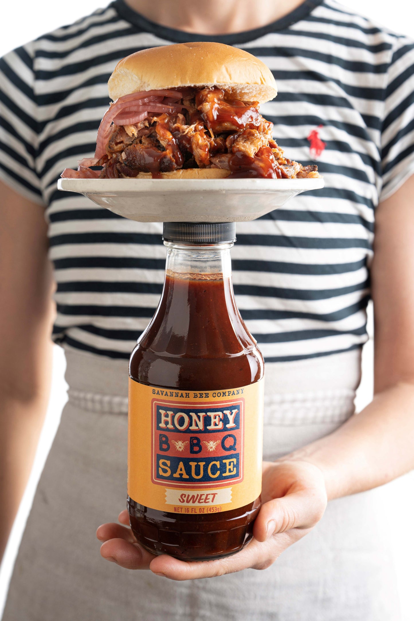 A BBQ sandwich with red onion balanced on a Savannah Bee Company sweet BBQ sauce