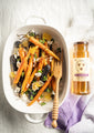 A bowl of full honey roasted carrots with feta, greens and honeycomb garnish next to a 12 ounce jar of tupelo honey.
