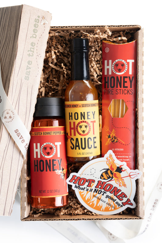 Gift box with Savannah Bee Company honey hot sauce, hot honey fire sticks, Hot Honey, and a hot honey sticker with a devil drone and flames. 