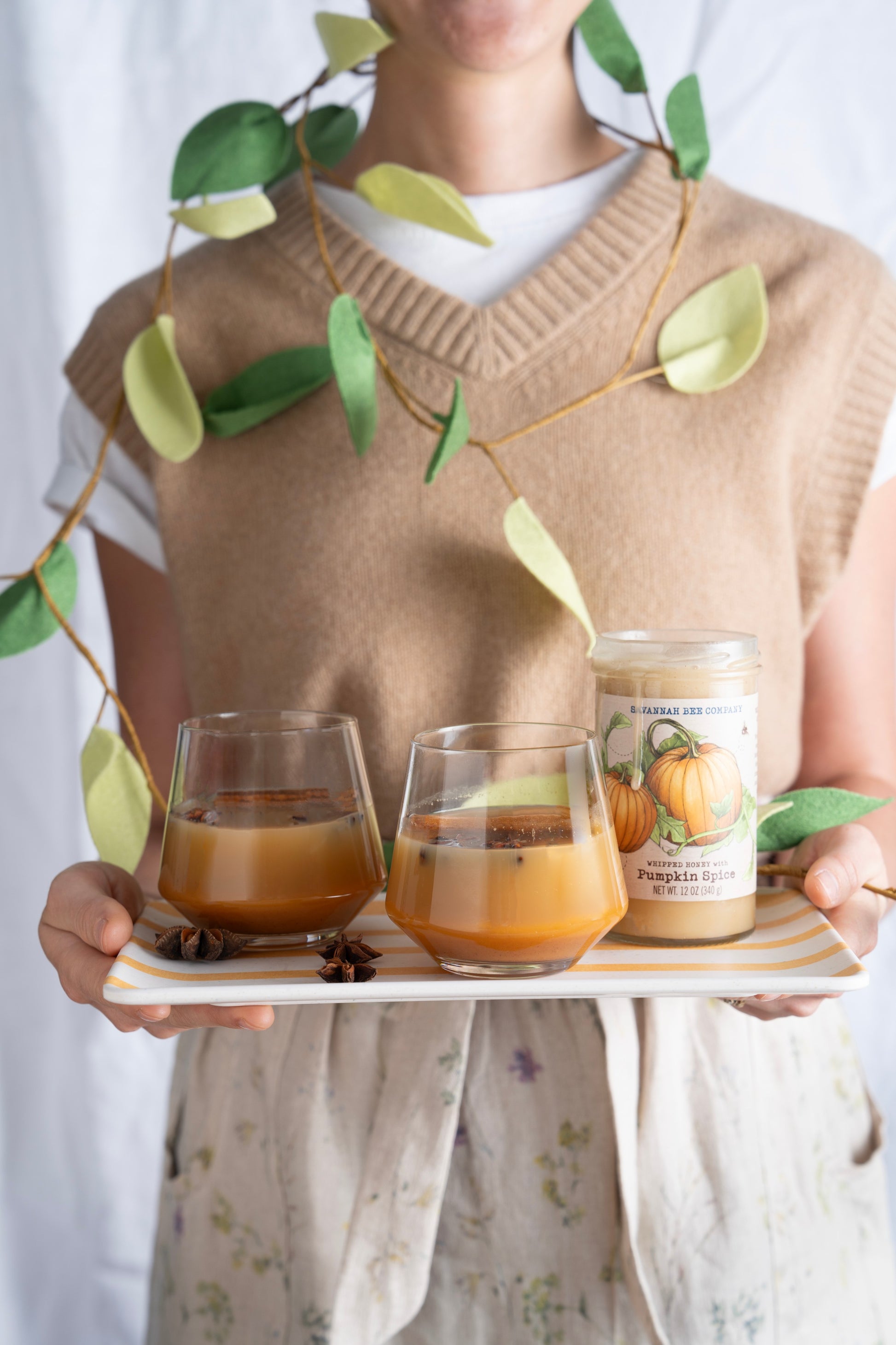 A woman holding a tray of pumpkin spice cider with an open jar of pumpkin spice whipped honey 12 ounce jar.