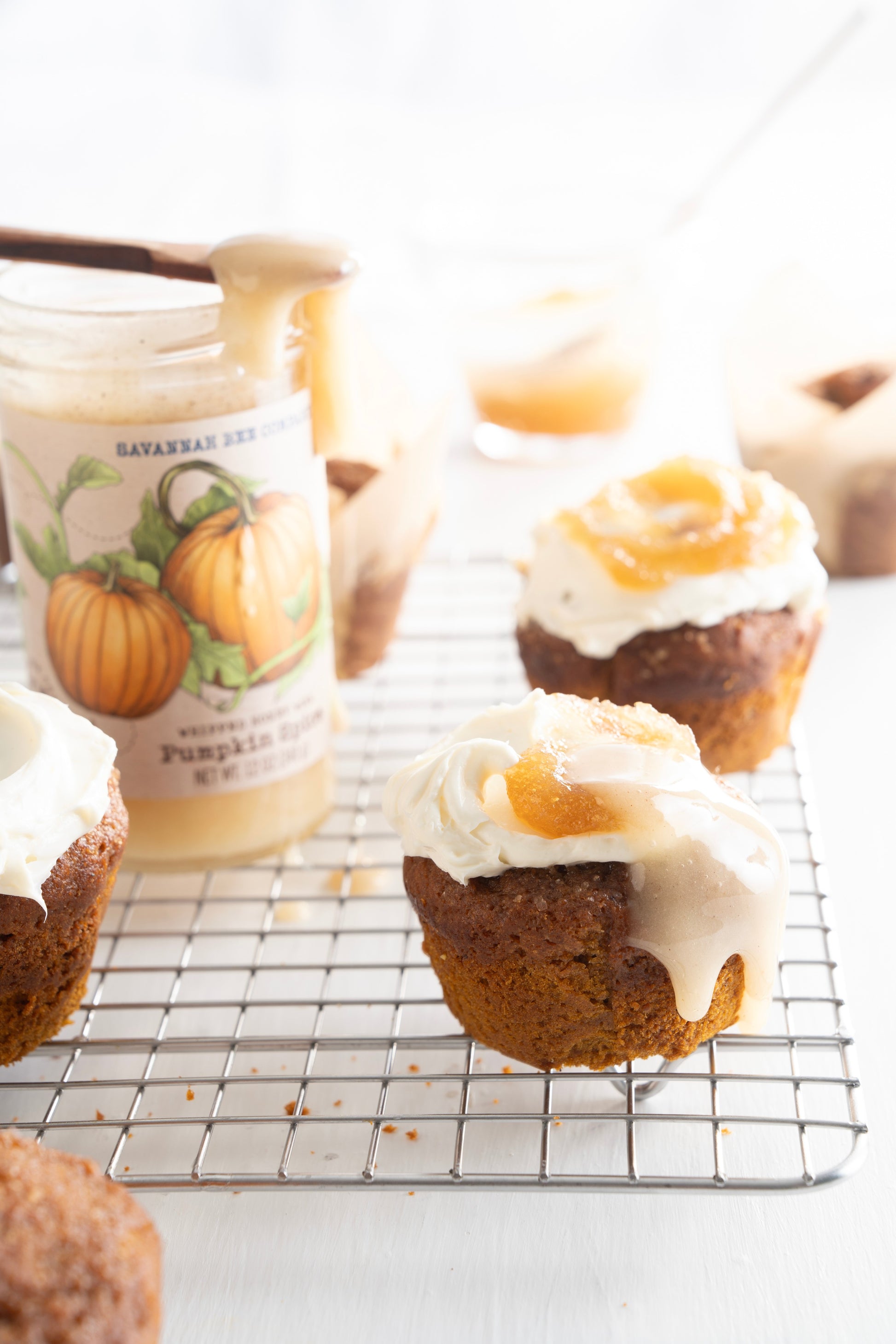 Pumpkin spice muffins with a pumpkin spice whipped honey glaze next to an open 12 ounce jar of pumpkin spice whipped honey.