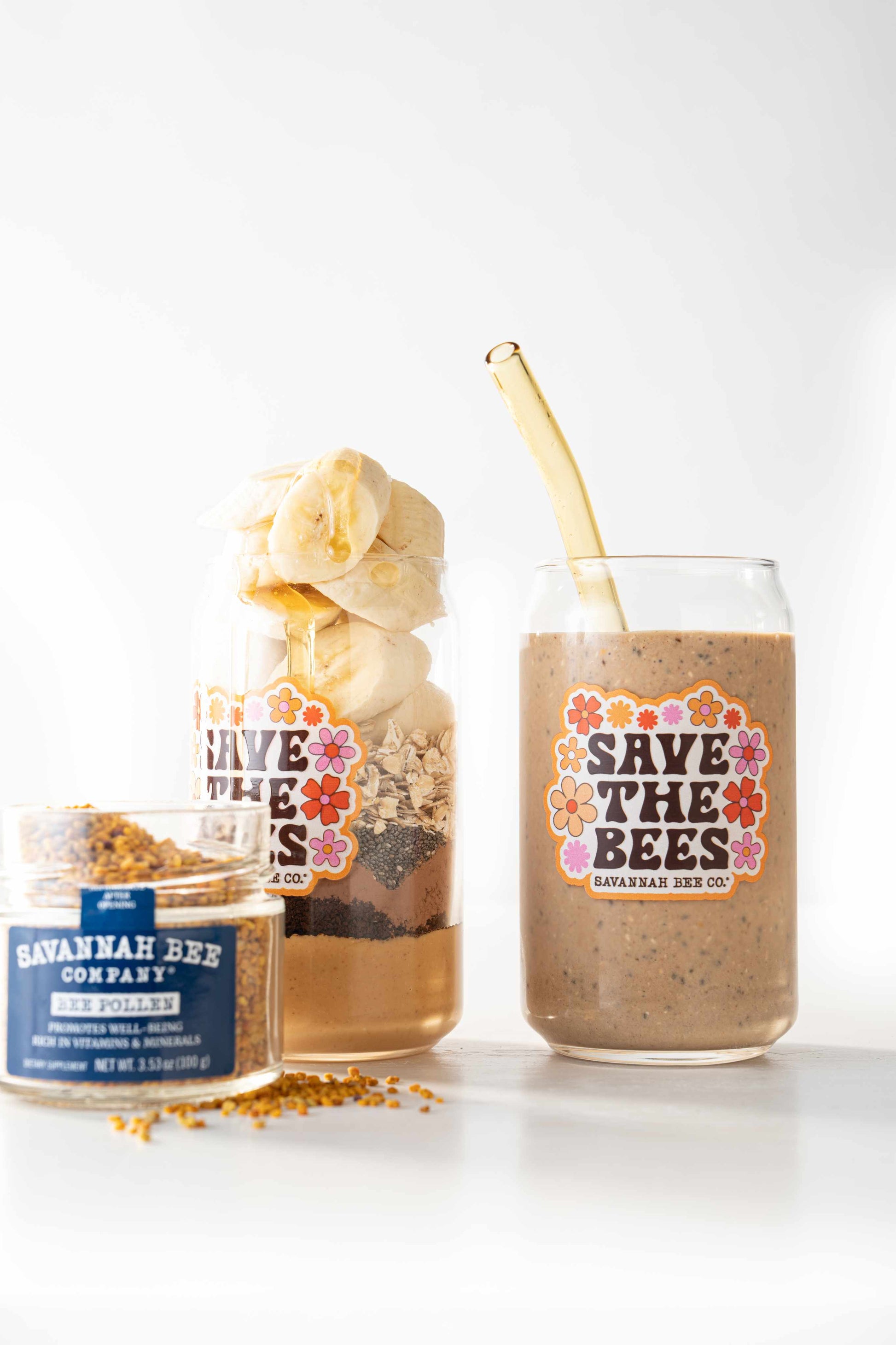 Save the bees glass can filled with a strawberry peanut butter and oats smoothie next to bee pollen and a glass of smoothie ingredients
