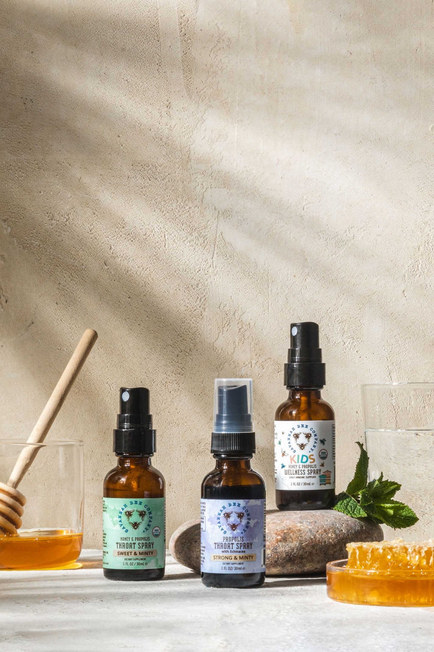 Kids Honey and Propolis Wellness Spray, Strong and Minty Proplois Spray and Sweet and Mint Propolis Spray next to honeycomb and dipper.