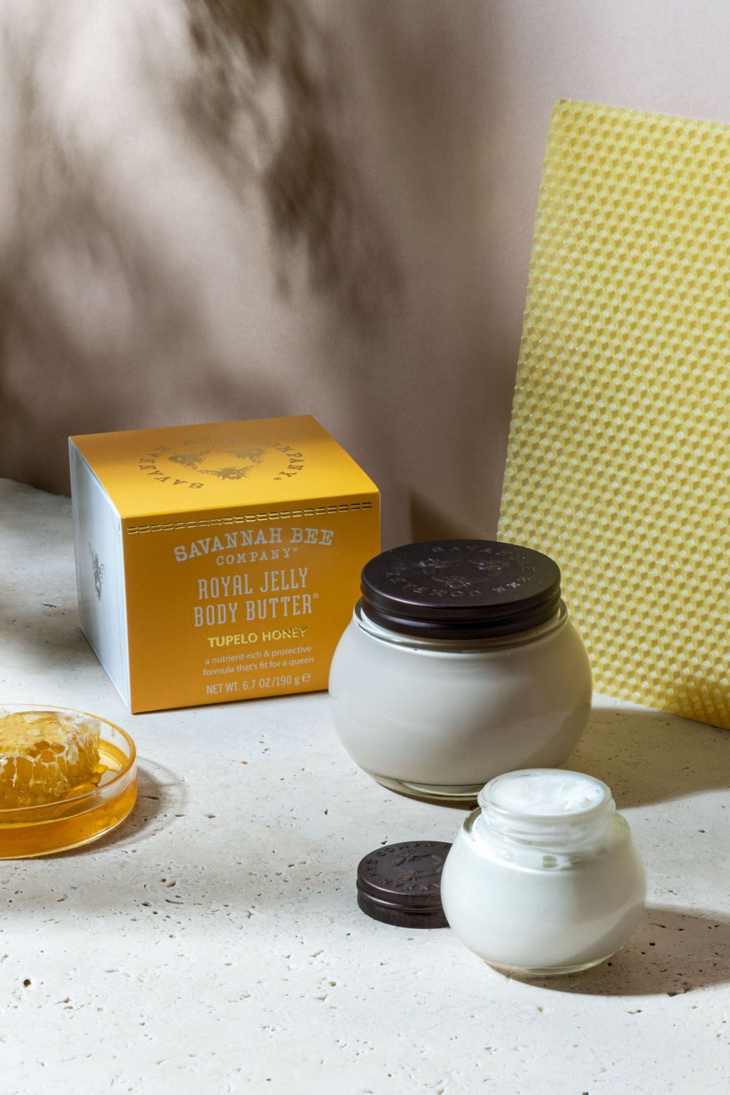 Small and large Royal Jelly Body Butter Tupelo Honey next to honeycomb