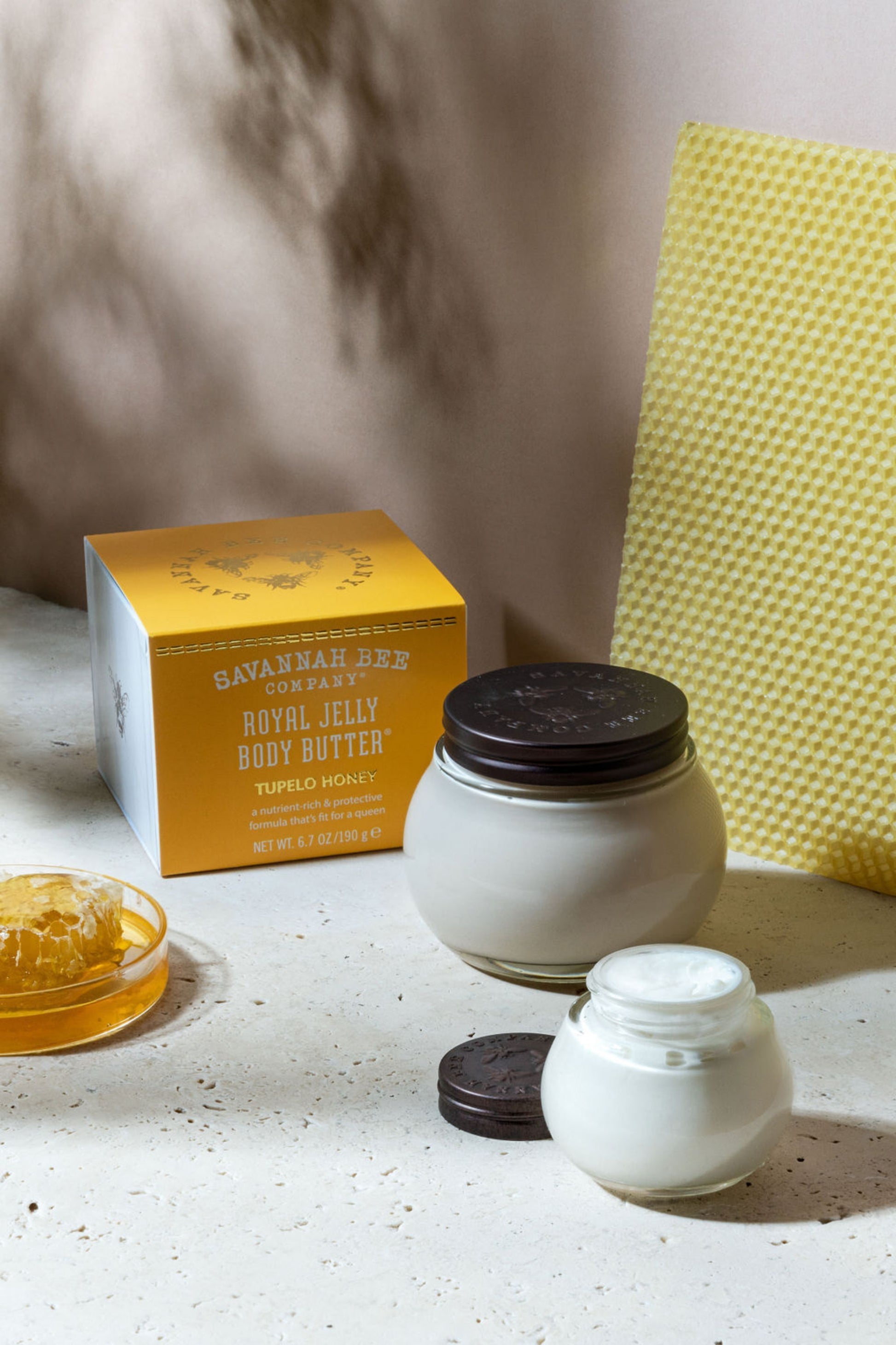 Small and large Royal Jelly Body Butter Tupelo Honey next to honeycomb