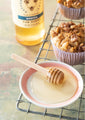 Mini honey dipper in a platter of honey next to a jar of acacia honey and a banana nut muffin.