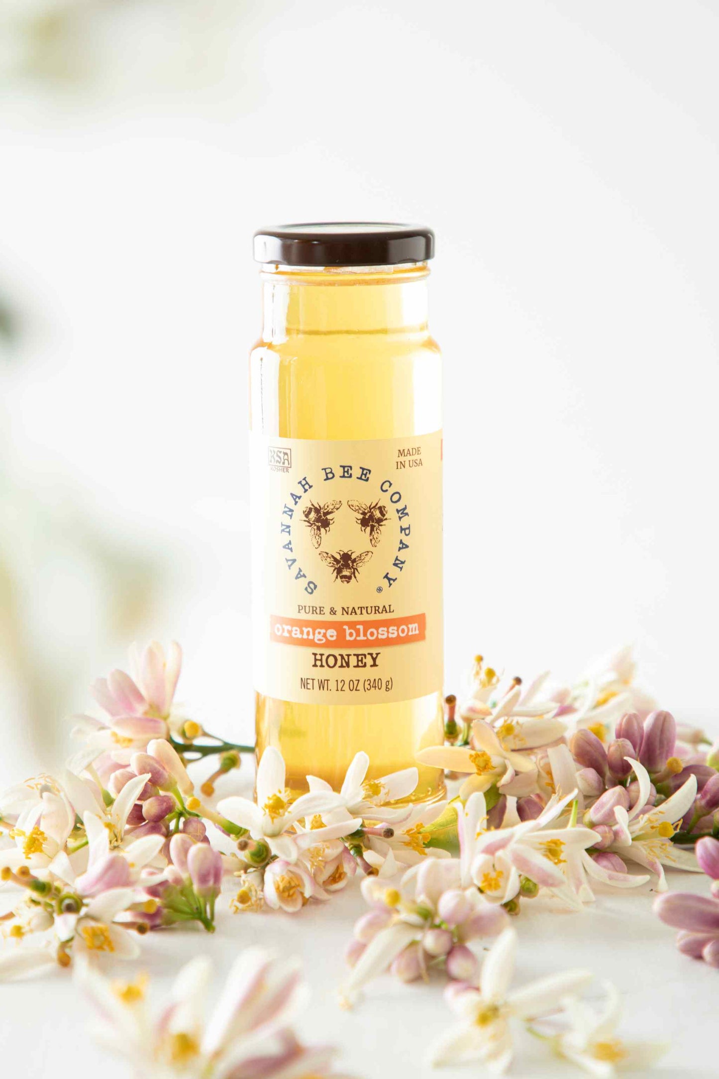 Pure & Natural Orange Blossom Honey 12 oz. tower surrounded by orange blossoms.