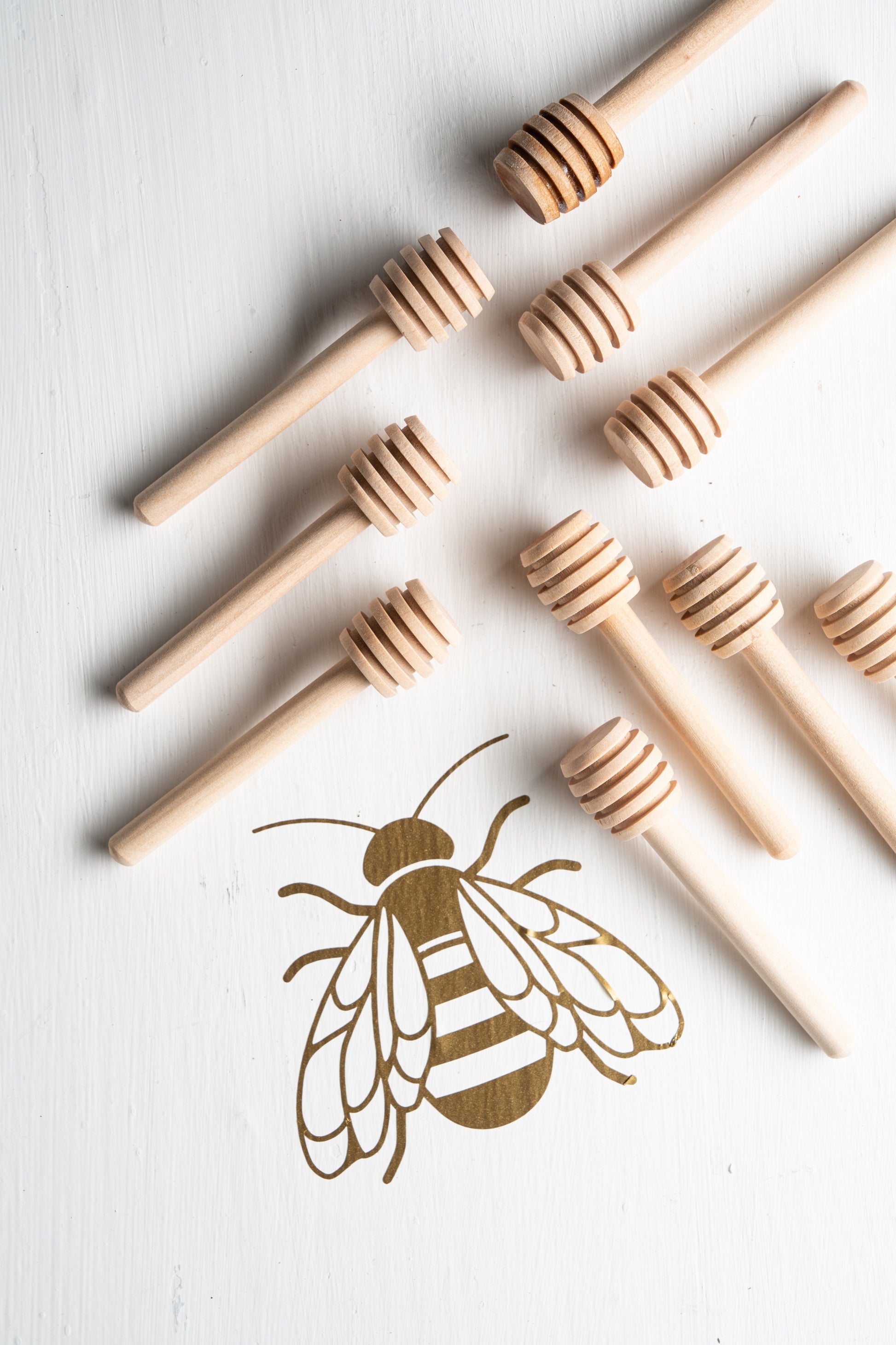 Ten mini honey dippers against a white background with a gold bee.