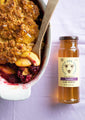 A tray of peach and blackberry cobbler next to a 12 ounce jar of tupelo honey.