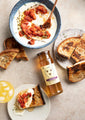 A plate of crostini and a bowl of whipped feta with sauteed tomatoes next to a 12 ounce jar of tupelo honey.