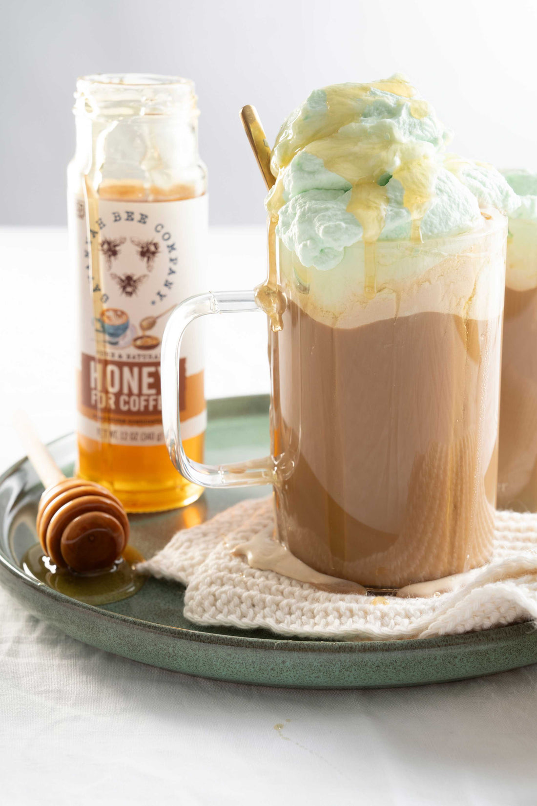 Coffee with green whipped cream on the top next to Honey for Coffee.