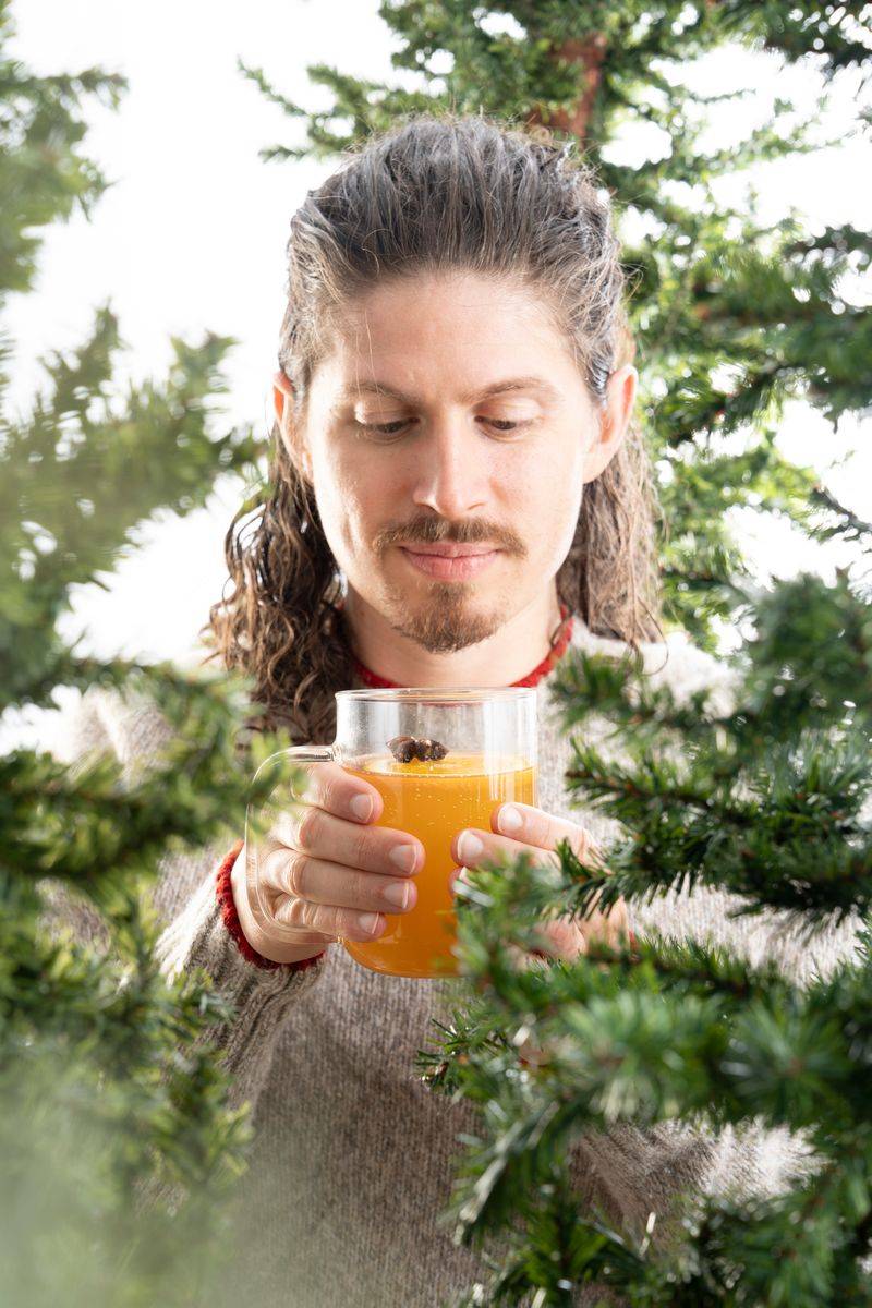 Man holding kombucha under a Christmas tree.