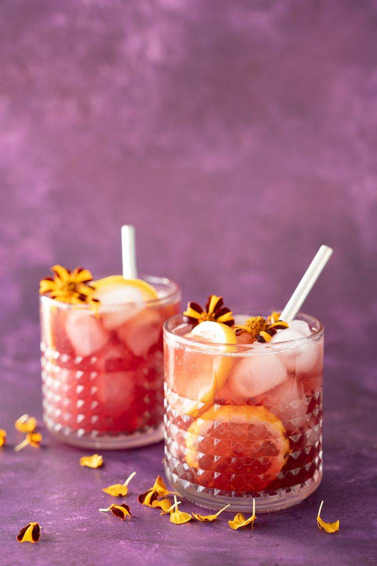 Tinto de Verano cocktail on a purple background with lemons and edible floral garnishes.