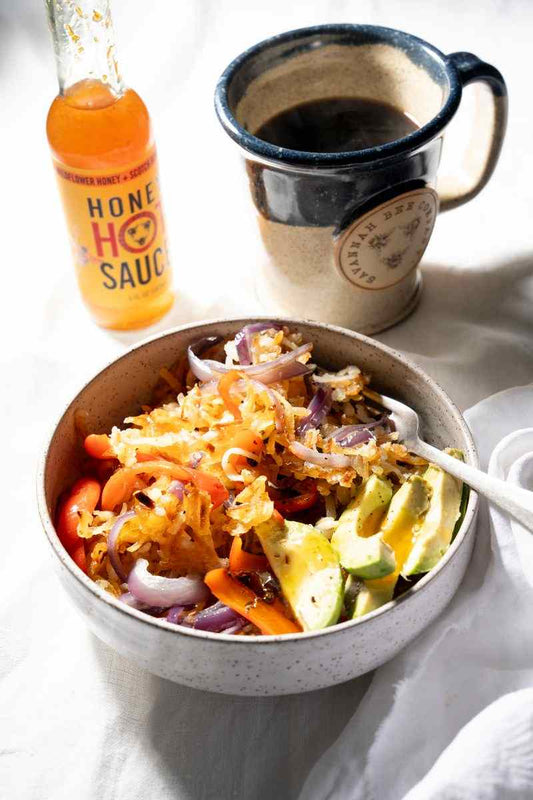 Hash browns and veggies next to Savannah Bee Company hot sauce and a mug of coffee. 