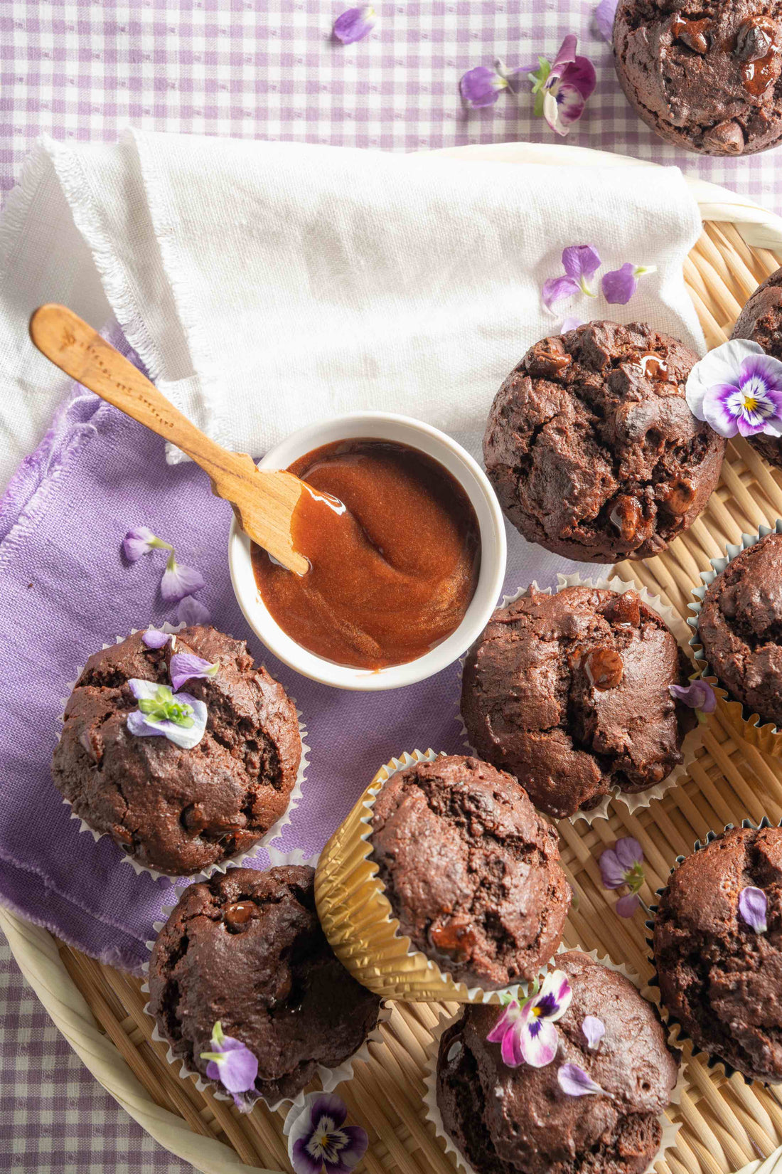 Triple chocolate muffins in a woven basket sitting on a purple gingham tablecloth and a bowl of Whipped Honey with Chocolate. 