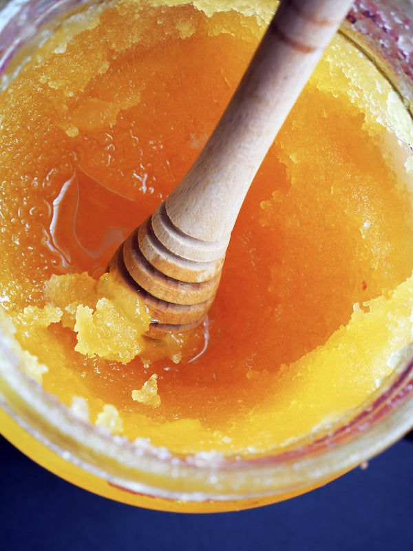 A jar of crystalized honey with a wooden dipper on top.
