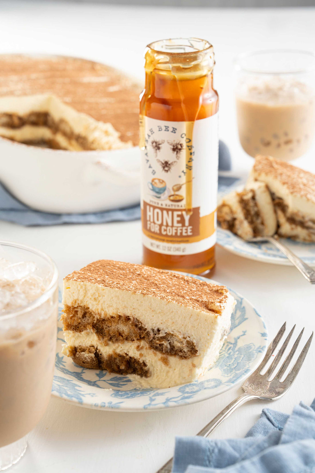 A slice of tiramisu next to a jar of honey for coffee.