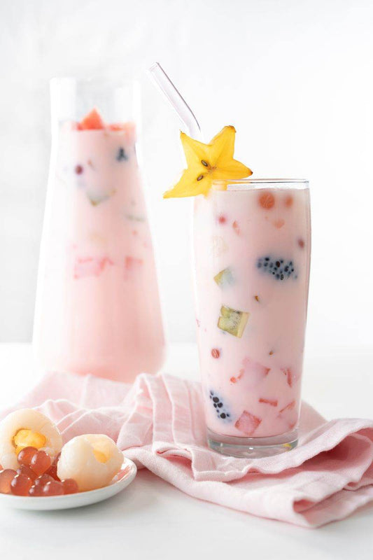 Korean Fruit Punch with strawberry milk in a glass filled with fruit next to a pitcher and a bowl of fruit