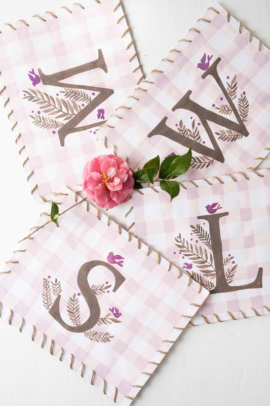 Pink gingham monogram placemats with brown lettering and a pink flower in the middle.