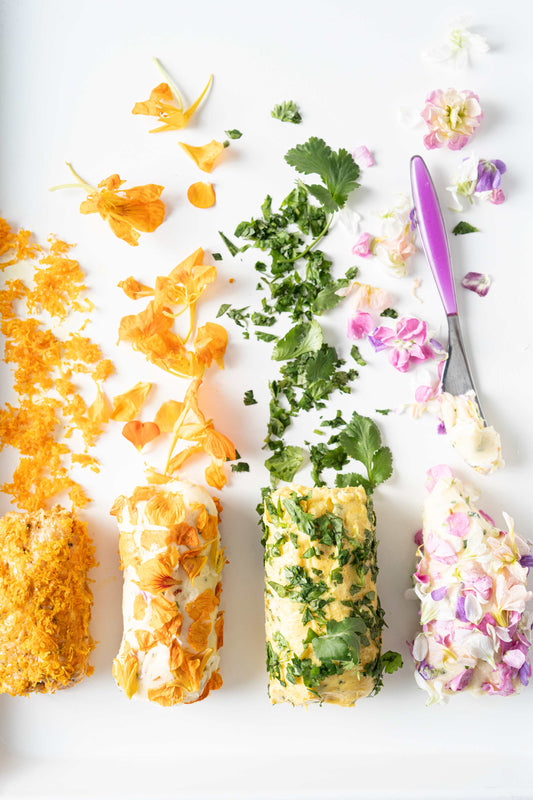 Honey compound butters coated with shredded orange zest, green herbs, and pink and white edible flower petals.
