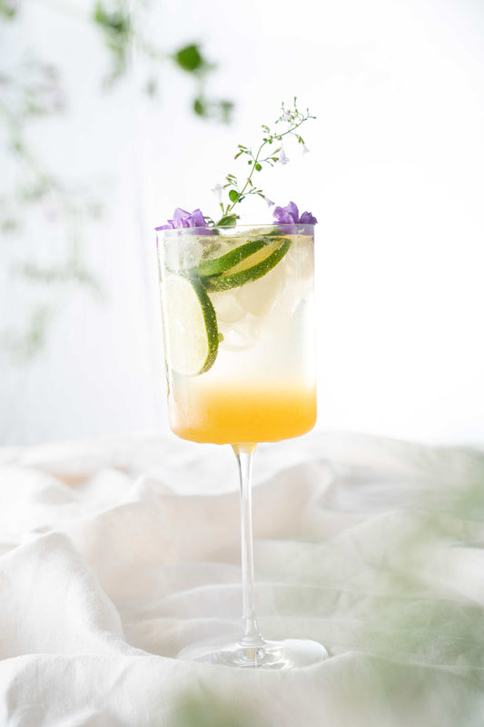 Honey hugo spritz cocktail garnished with lime and edible flowers.