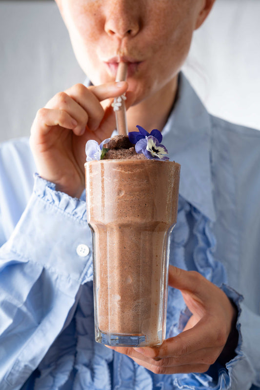 A woman drinking a frozen Mexican hot chocolate with a flower garnish from a straw.