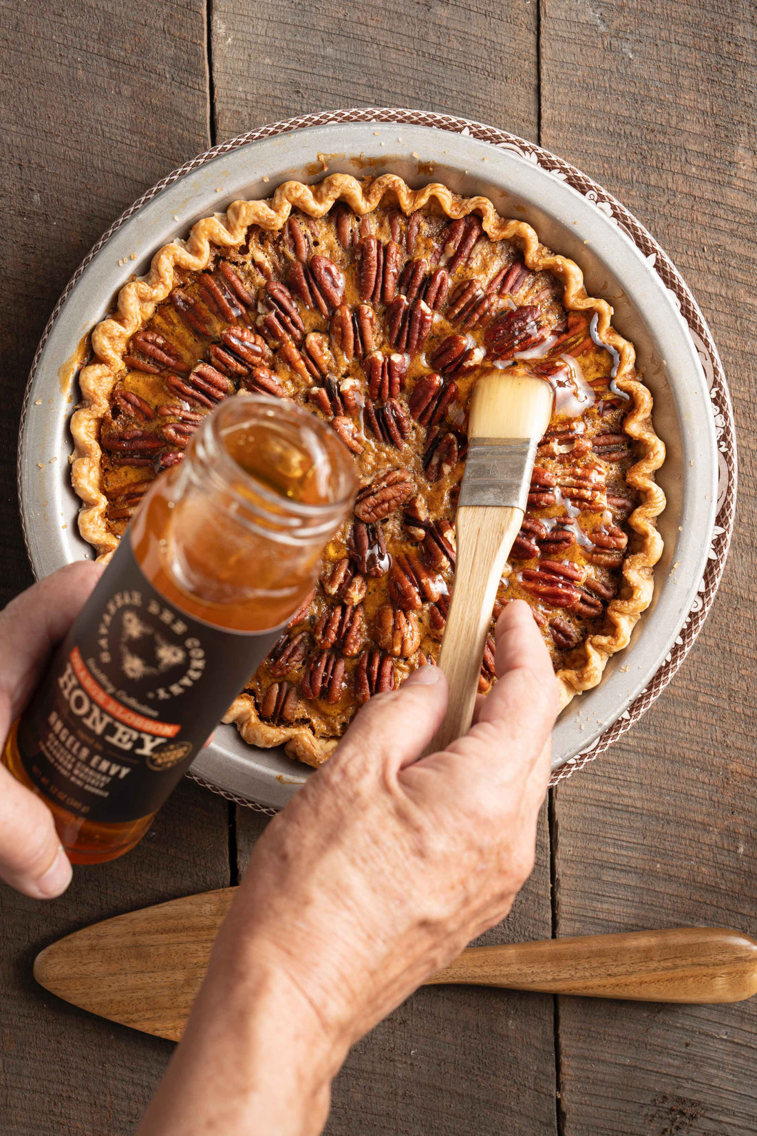 A hostess uses a brush to coat a pecan pie with bourbon honey from a 12oz jar of Savannah Bee Company Bourbon Honey.