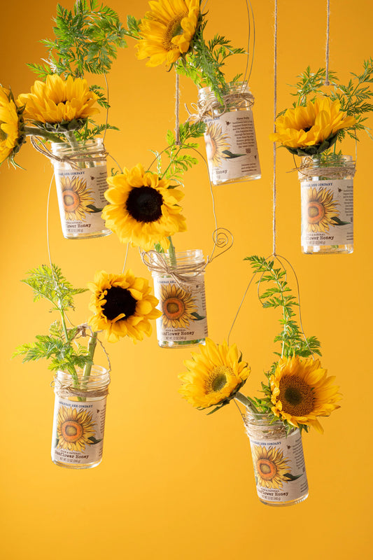 Sunflowers in hanging honey jars against a yellow background.