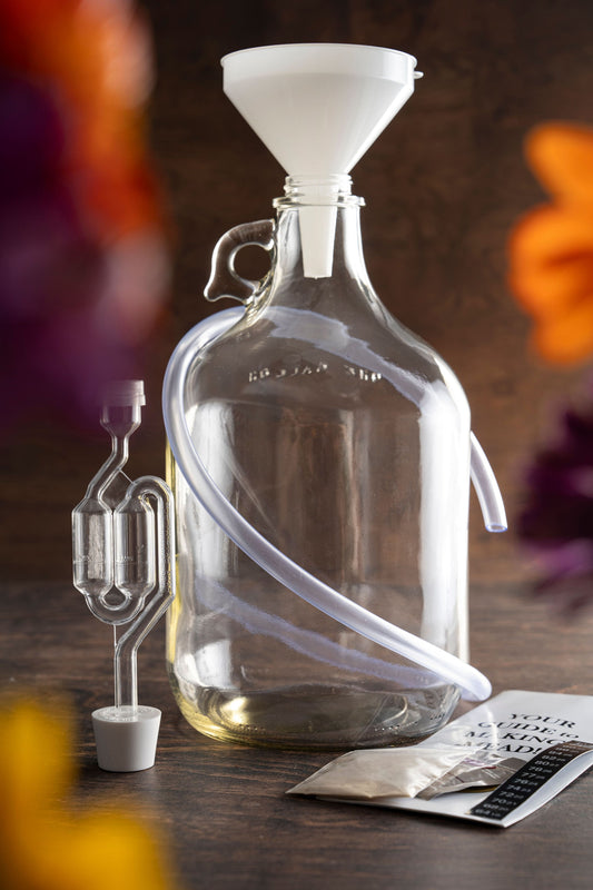 Flower background, Savannah Bee Company Mead Making Kit includes a 1 gallon glass carboy, airlock and rubber stopper, syphon tube, thermometer tape, yeast, yeast nutrients, funnel and step-by-step instructions.