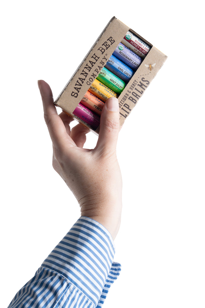 Hand holding a box of savannah bee company lip balms on a white background