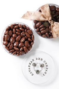 Two tins of chocolate covered honey crisp pecans against a white background with a ribbon.