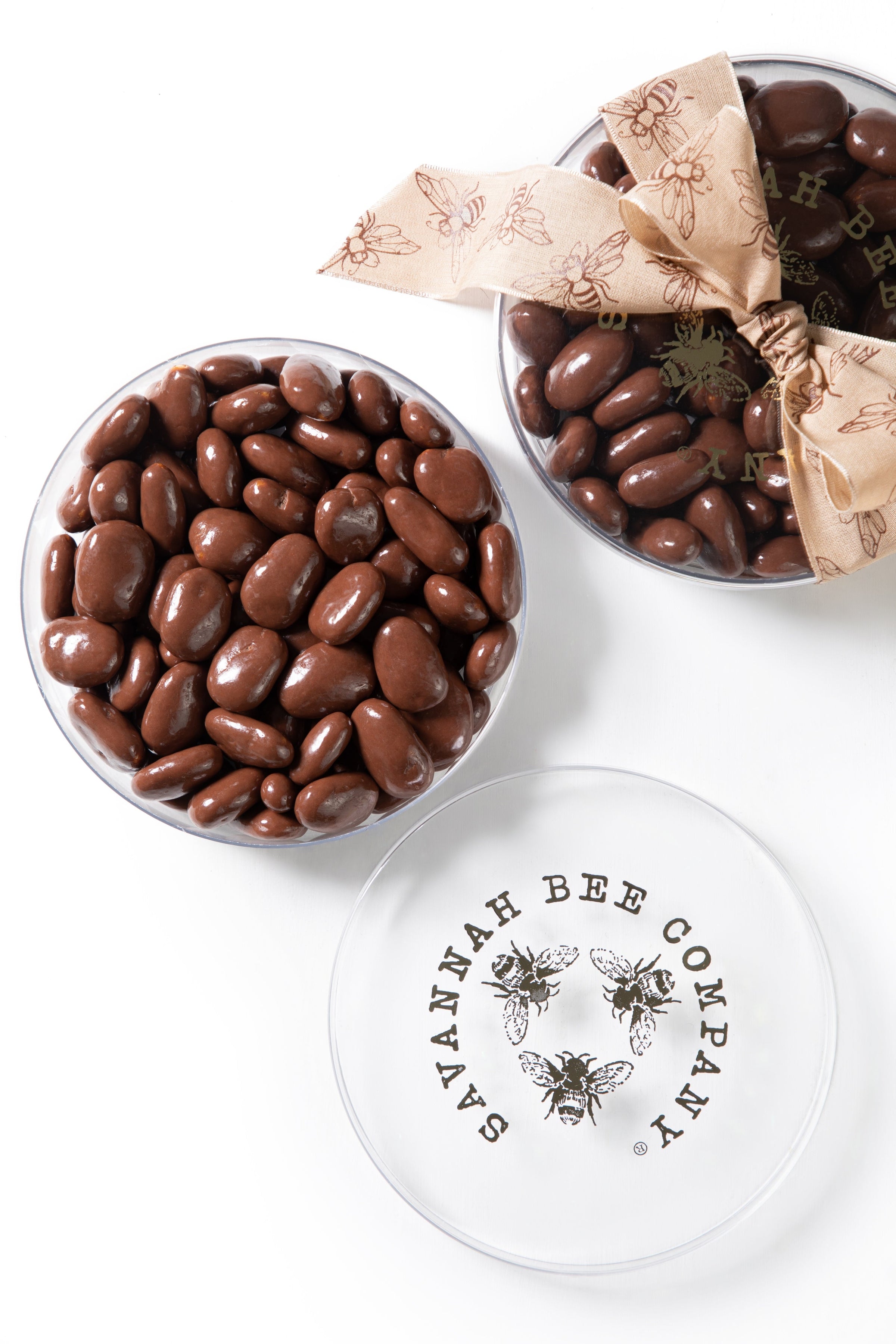 Two tins of chocolate covered honey crisp pecans against a white background with a ribbon.