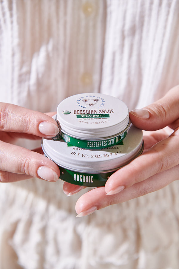 Large and mini Beeswax salve, spearmint stacked on top of one another in someones hands