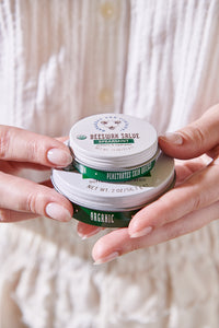 Large and mini Beeswax salve, spearmint stacked on top of one another in someones hands