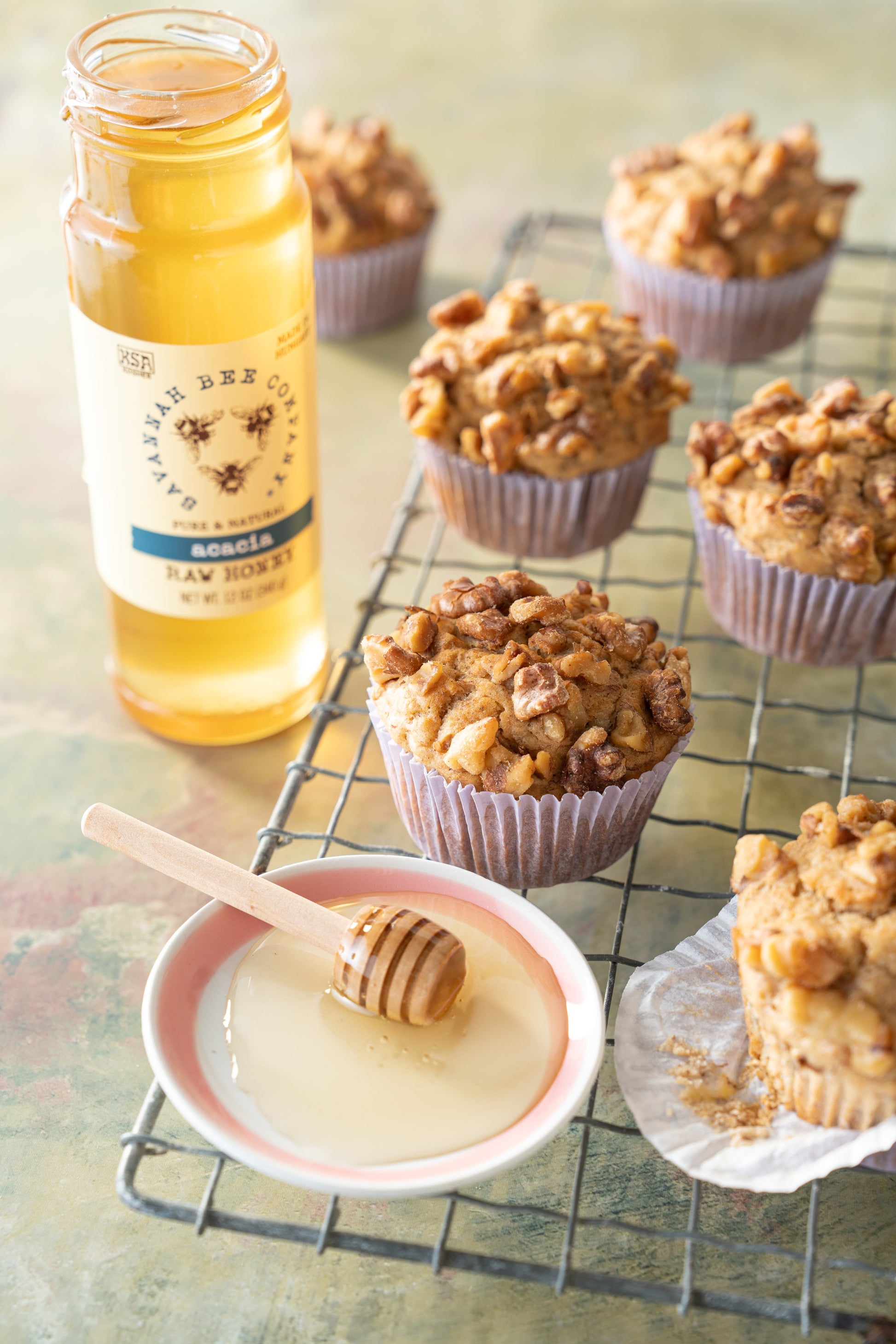 Banana spice muffins on an oven rack with an open jar of 12 ounce acacia honey.
