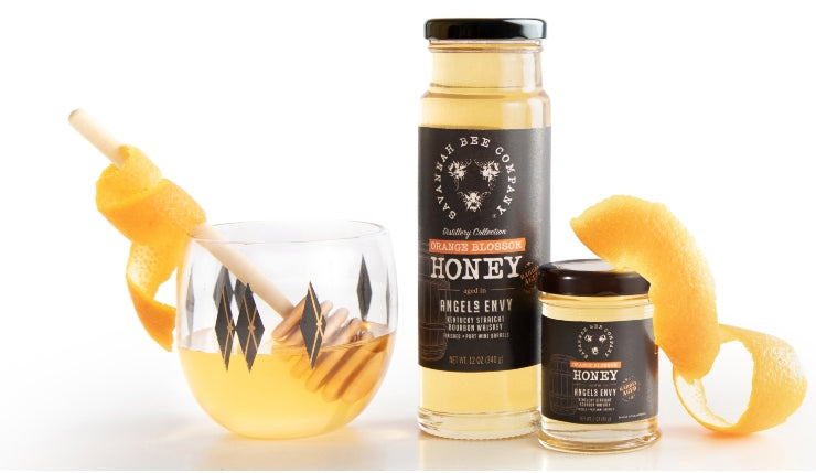 12oz and 3oz Orange Blossom Honey with Savannah Bee Logo. Surround by a cocktail glass, wooden honey dipper and orange zest.