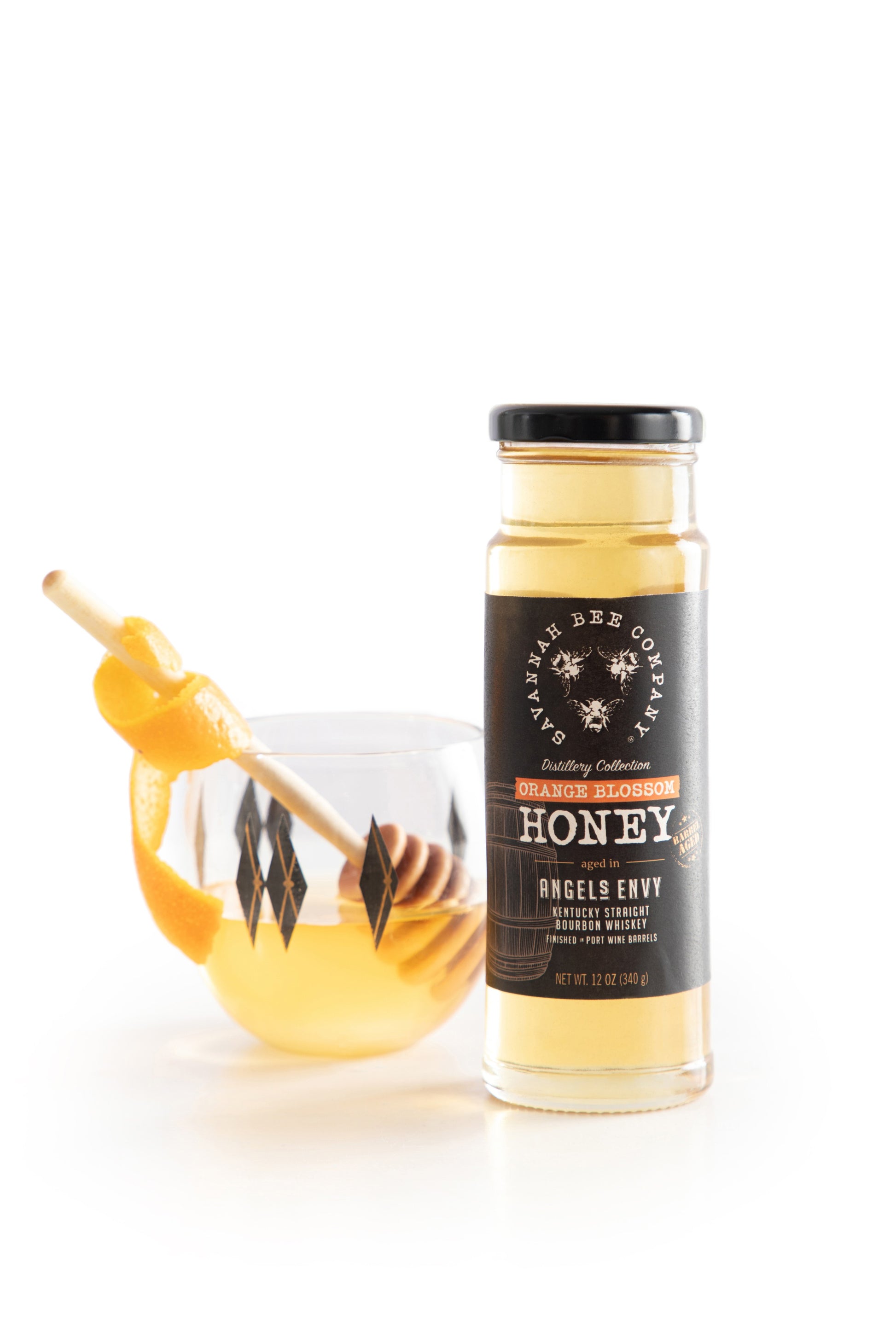 12 ounce Port Bourbon Barrel Aged Orange Blossom Honey next to a bourbon cocktail against a white background.