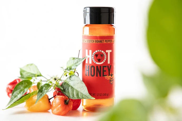 Hot Honey Squeeze Bottle surround by scotch bonnet peppers and leafs